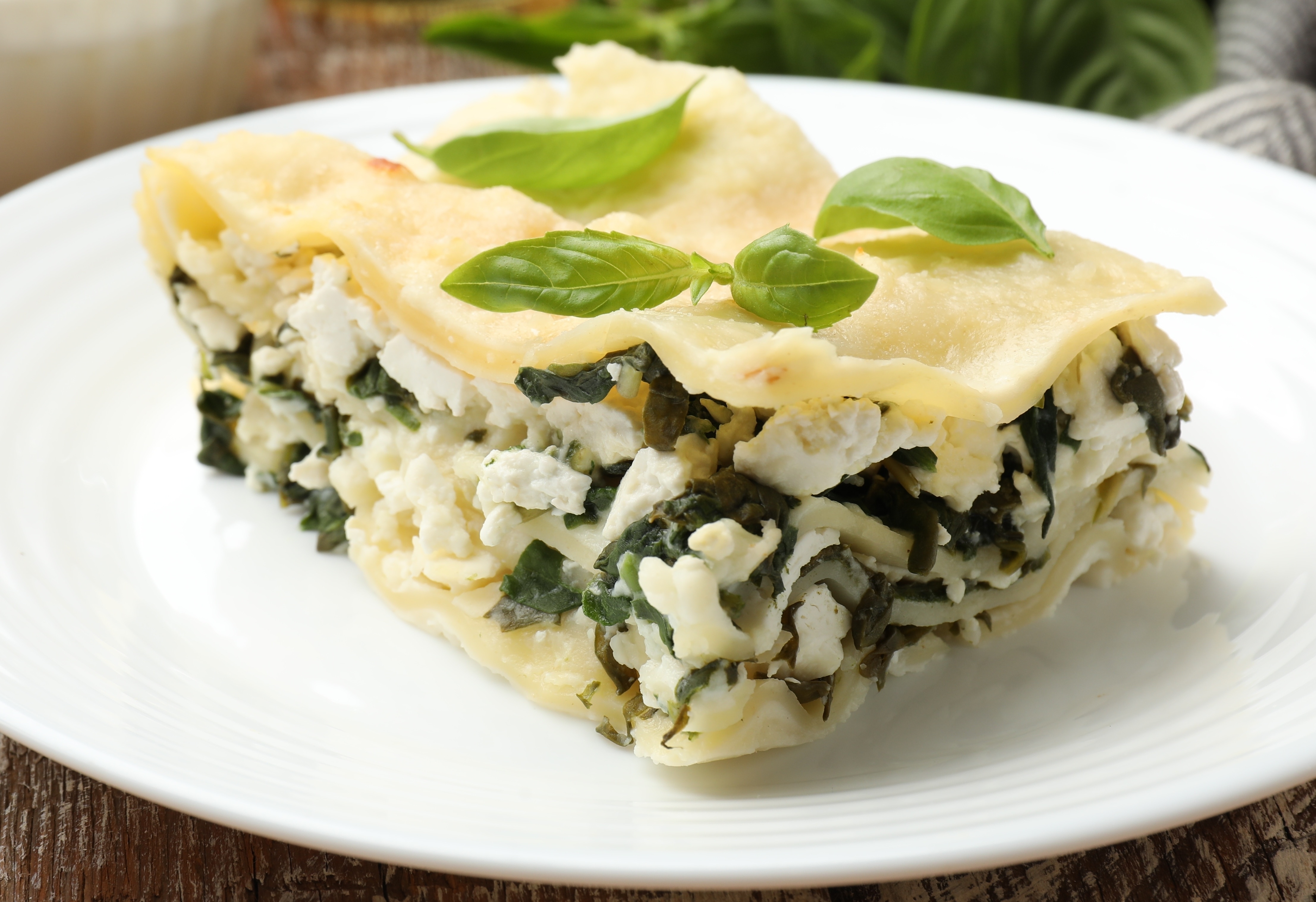 Piece of tasty vegetarian lasagna and ingredients on wooden table, closeup